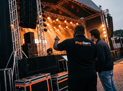 Equipe Pop Som de uniforme preto diante de um palco com a iluminação acesa